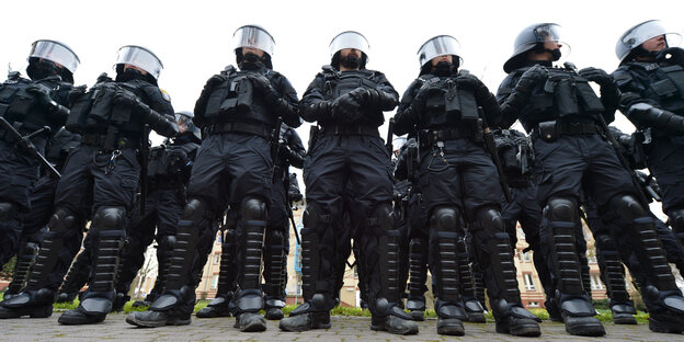 Polizisten in blauen Overalls mit Brustschutz, Schienbeinschutz, Handschuhen und Helmen mit herunter geklapptem Visier. Polizisten in blauen Overalls mit Brustschutz, Schienbeinschutz, Handschuhen und Helmen mit herunter geklapptem Visier.