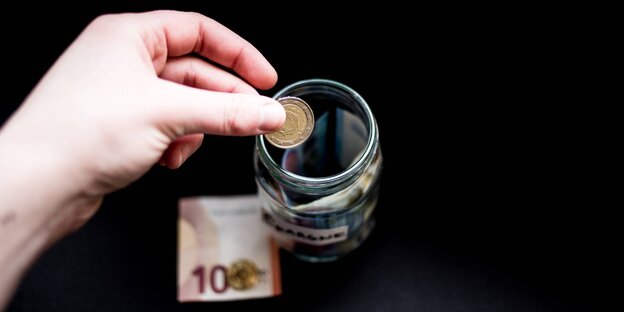 Jemand wirft zwei Euro in ein Glas Jemand wirft zwei Euro in ein Glas