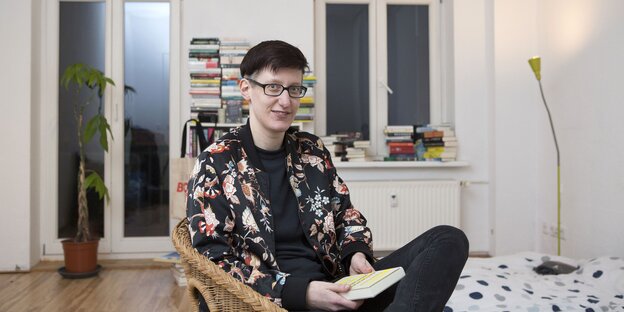 Eine Person sitzt in einem Korbsessel. In der Hand hat sie ein Buch