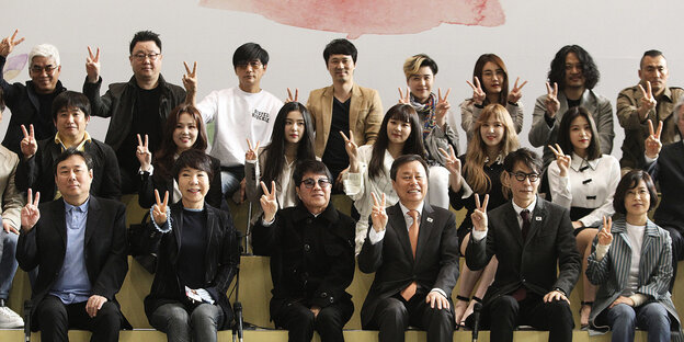 Südkoreanische Popstars, in drei Reihen hintereinander sitzend - alle machen das Victory-Zeichen Südkoreanische Popstars, in drei Reihen hintereinander sitzend - alle machen das Victory-Zeichen