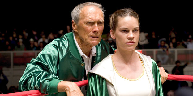 Clint Eastwood steht neben Hilary Swank, die im Boxring steht Clint Eastwood steht neben Hilary Swank, die im Boxring steht
