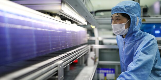 Chinesische Mitarbeiterin mit Schutzkleidung in Solarfabrik in China starrt konzentriert auf ein Solarpanel Chinesische Mitarbeiterin mit Schutzkleidung in Solarfabrik in China starrt konzentriert auf ein Solarpanel