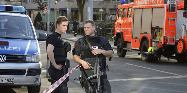 Polizisten auf einer Straße, im Hintergrund ein Feuerwehrwagen Polizisten auf einer Straße, im Hintergrund ein Feuerwehrwagen