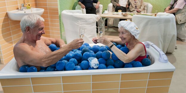 Eine Seniorin und ein Senior sitzen gemeinsam in einer Badewanne voller Plastikbälle. Eine Seniorin und ein Senior sitzen gemeinsam in einer Badewanne voller Plastikbälle.