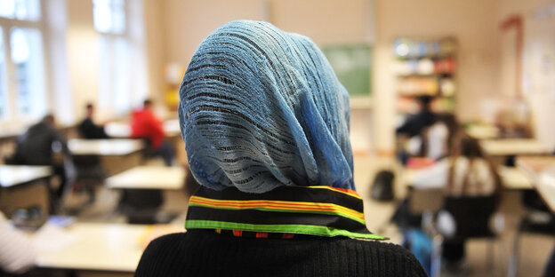 Ein Mädchen mit Kopftuch steht in einer Schule vor einem Klassenzimmer Ein Mädchen mit Kopftuch steht in einer Schule vor einem Klassenzimmer