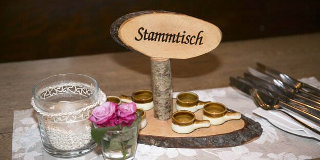 Ein Holzschild auf dem „Stammtisch“ steht, danben Gläser und Besteck Ein Holzschild auf dem „Stammtisch“ steht, danben Gläser und Besteck