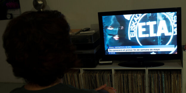 Eine Frau schaut auf einen Fernseher, in dem das Symbol der ETA zu sehen ist. Eine Frau schaut auf einen Fernseher, in dem das Symbol der ETA zu sehen ist.