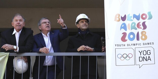 Drei Männer stehen auf einer Baustelle, neben ihnen hängt ein Plakat der Olympischen Jugendspiele Drei Männer stehen auf einer Baustelle, neben ihnen hängt ein Plakat der Olympischen Jugendspiele