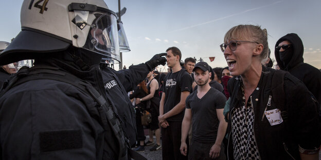 Polizisten mit Helm stehen vor schreiender Demonstrantin Polizisten mit Helm stehen vor schreiender Demonstrantin