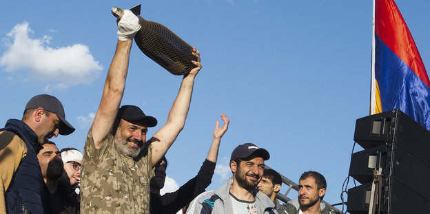 Ein Mann hält eine Riesenflasche in die Höhe, umstanden von anderen Männern, rechts im Bildrand die armenische Fahne