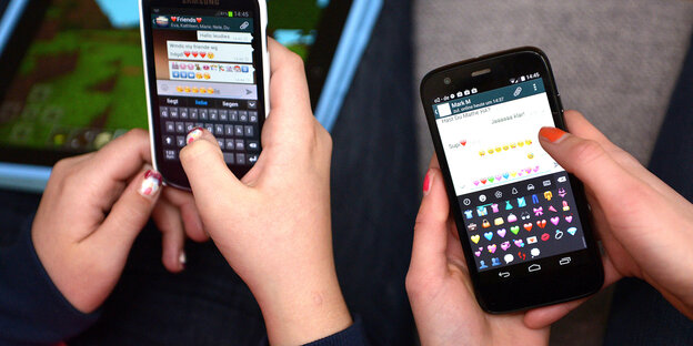 Zwei Teenager halten Smartphones in den Händen, auf denen sie den Messengerdienst WhatsApp benutzen Zwei Teenager halten Smartphones in den Händen, auf denen sie den Messengerdienst WhatsApp benutzen