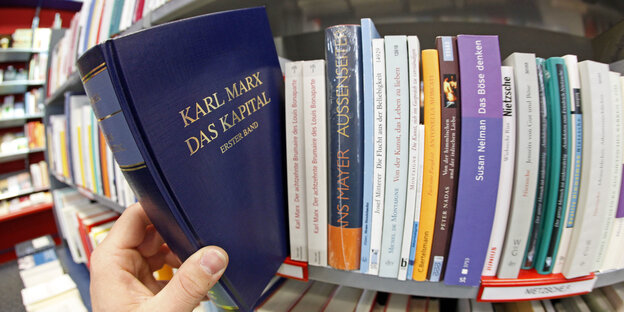 Jemand nimmt das blaue Buch „Das Kapital" von Karl Marx aus einem Regal Jemand nimmt das blaue Buch „Das Kapital" von Karl Marx aus einem Regal