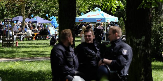 Polizisten in einem Park, im Hintergrund kleine Festpavillons Polizisten in einem Park, im Hintergrund kleine Festpavillons