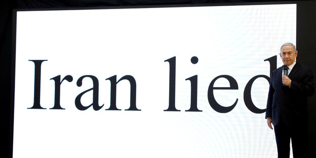 Ein Mann mit grauen Haaren steht vor einer Leinwand, auf der wird in großen Buchstaben angestrahlt: "Iran lied" Ein Mann mit grauen Haaren steht vor einer Leinwand, auf der wird in großen Buchstaben angestrahlt: "Iran lied"