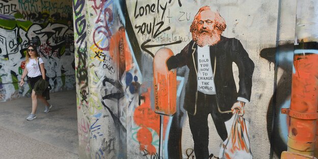 Ein Graffiti zeigt einen Mann, der in einen Mülleimer greift und eine Plastiktüte hält, im Hintergrund läuft eine Frau vorbei Ein Graffiti zeigt einen Mann, der in einen Mülleimer greift und eine Plastiktüte hält, im Hintergrund läuft eine Frau vorbei