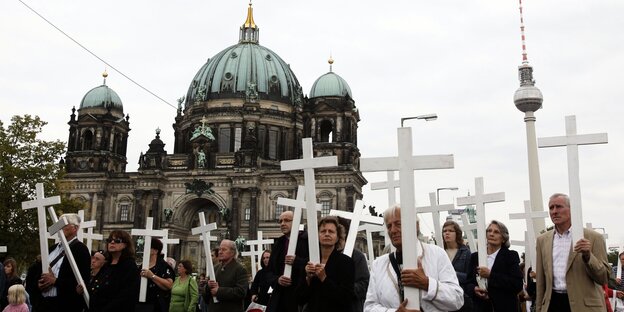Mehrere Menschen laufen nebeneinander und halten weiße Kreuze hoch Mehrere Menschen laufen nebeneinander und halten weiße Kreuze hoch