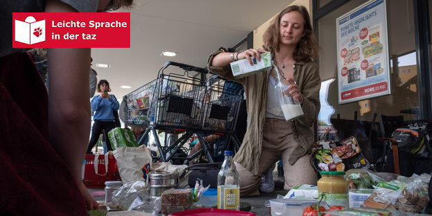 Eine Frau sitzt auf einem Supermarktboden und füllt Milch aus einer Milchpackung in eine Glasflasche um Eine Frau sitzt auf einem Supermarktboden und füllt Milch aus einer Milchpackung in eine Glasflasche um