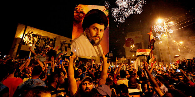 Eine Menschenmenge, in der ein Mann ein Porträgt von Muktada a-Sadr in die Höhe hält Eine Menschenmenge, in der ein Mann ein Porträgt von Muktada a-Sadr in die Höhe hält