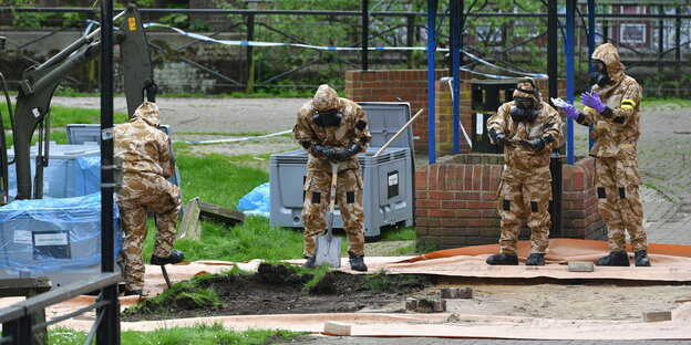 Vier Männer in Militärkleidung und Schutzmasken untersuchen den Boden. Im Hintergrund große graue Boxen. Vier Männer in Militärkleidung und Schutzmasken untersuchen den Boden. Im Hintergrund große graue Boxen.