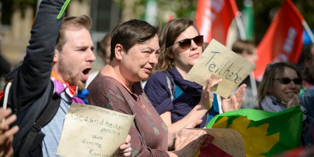 Mehrere Menschen halten Schilder in die Höhe, auf denen „Teilhabe statt Hartz IV“ und "Gesundheitspolitik statt dumme Kommentare" steht