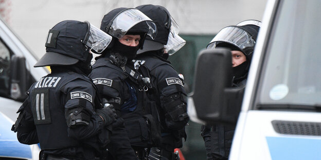 Drei Polizisten stehen in voller Montur vor einem Polizeibus Drei Polizisten stehen in voller Montur vor einem Polizeibus