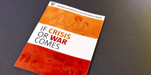 Eine Broschüre in orange, rot und weiß mit der englischsprachigen Aufschrift "Falls Krise oder Krieg kommt" liegt auf einem Tisch