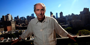 Philip Roth steht unter strahlend blauem Himmel vor der Skyline New Yorks