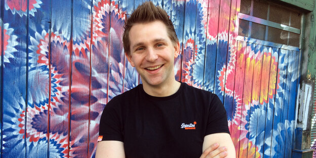 Max Schrems mit verschränkten Armen vor einer bunten Streetart-Wand