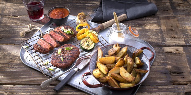 Ein Tablett auf einem Holztisch, darauf ein Steak, Pommes und andere Lebensmittel Ein Tablett auf einem Holztisch, darauf ein Steak, Pommes und andere Lebensmittel