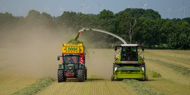 Eine Mähmaschine befüllt einen Transporter bei der Fahrt übers Feld Eine Mähmaschine befüllt einen Transporter bei der Fahrt übers Feld
