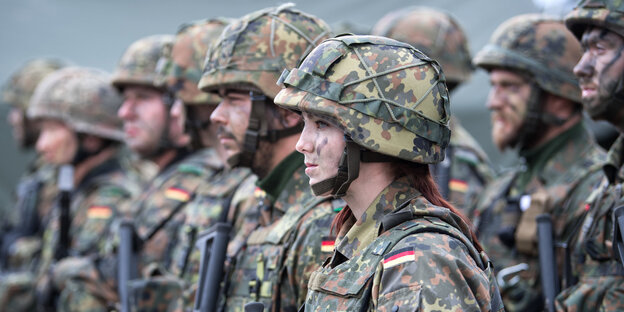 Mehrere Soldaten und Soldatinnen stehen in Reihen. Sie haben Helme und Uniform an und sind mit Farbe im Gesicht angemalt Mehrere Soldaten und Soldatinnen stehen in Reihen. Sie haben Helme und Uniform an und sind mit Farbe im Gesicht angemalt