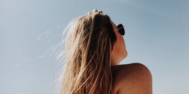 Eine Frau trägt Sonnenbrille und guckt in den blauen Himmel Eine Frau trägt Sonnenbrille und guckt in den blauen Himmel