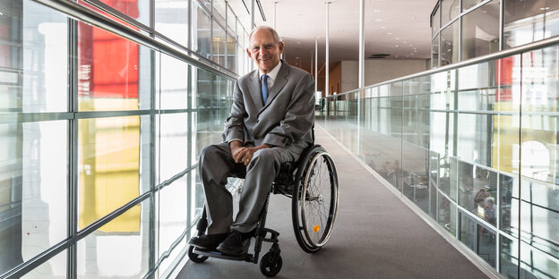 Wolfgang Schäuble, ein deutscher Politiker im Rollstuhl, wartet in einem Gang und lächelt. Wolfgang Schäuble, ein deutscher Politiker im Rollstuhl, wartet in einem Gang und lächelt.