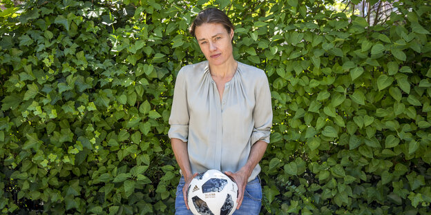 Katja Kraus steht vor einer Hecke und hält einen Fußball in den Händen Katja Kraus steht vor einer Hecke und hält einen Fußball in den Händen