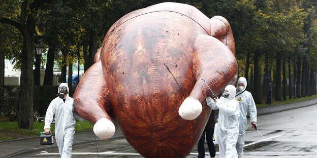 Drei Demonstranten in weißen Schutzanzügen tragen ein riesiges, aufblasbares Hähnchen Drei Demonstranten in weißen Schutzanzügen tragen ein riesiges, aufblasbares Hähnchen