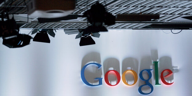 Der bunte Google Schriftzug an einer weißen Wand, darüber Scheinwerfer an der Decke Der bunte Google Schriftzug an einer weißen Wand, darüber Scheinwerfer an der Decke