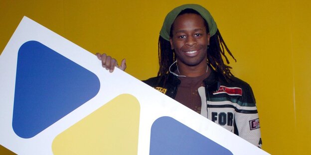 Mola Adebisi hält lächelnd ein Viva-Logo in der Hand Mola Adebisi hält lächelnd ein Viva-Logo in der Hand