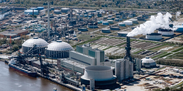 An einem Fluss steht ein großes Kraftwerk mit zwei runden Gebäuden und einem Schornstein, aus dem weißer Rauch kommt An einem Fluss steht ein großes Kraftwerk mit zwei runden Gebäuden und einem Schornstein, aus dem weißer Rauch kommt