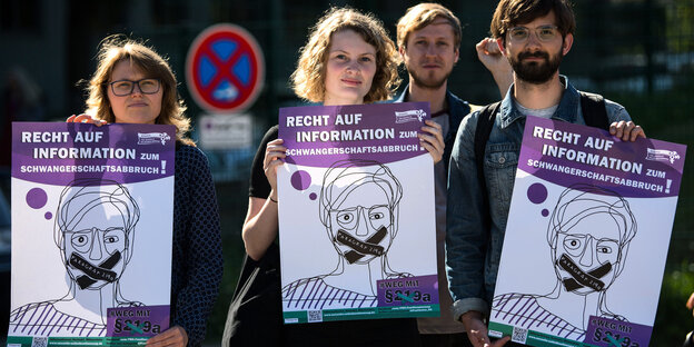 Zwei Frauen und ein Mann halten Plakate hoch, auf denen eine Person zu sehen ist, deren Mund zugeklebt ist. Auf dem Klebeband steht "Paragraf 219a" Zwei Frauen und ein Mann halten Plakate hoch, auf denen eine Person zu sehen ist, deren Mund zugeklebt ist. Auf dem Klebeband steht "Paragraf 219a"