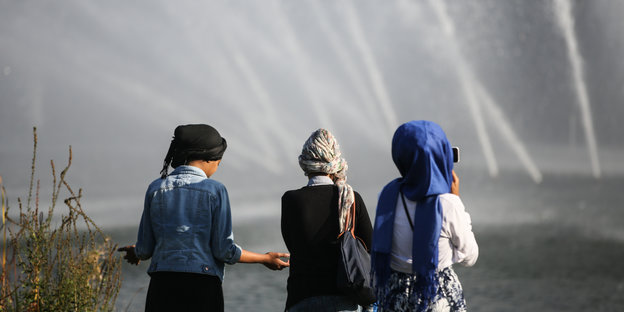 Drei Mädchen mit Kopftüchern stehen vor Wasserfontänen
