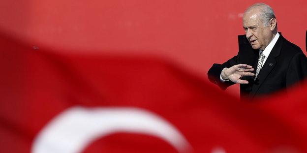 Devlet Bahçeli mit abwehrender Handgeste vor einer Türkeiflagge