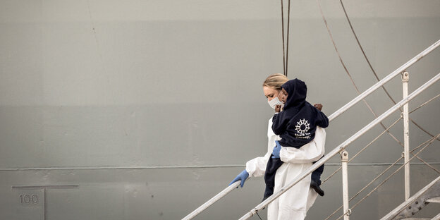 Eine Frau trägt ein Kleinkind vom Schiff Eine Frau trägt ein Kleinkind vom Schiff