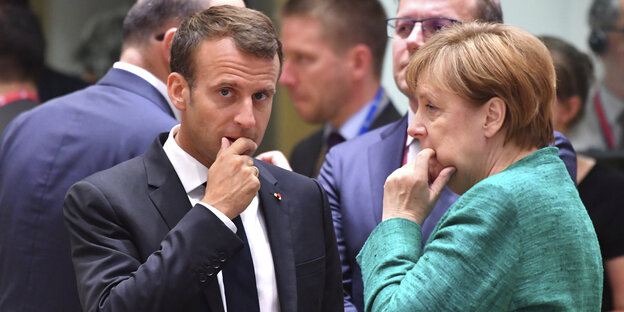 Merkel und Marcron stehen zusammen, beide haben die rechte Hand ans Kinn gelegt Merkel und Marcron stehen zusammen, beide haben die rechte Hand ans Kinn gelegt
