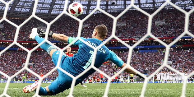 ein Torhüter durchs Tornetz von hinten, der mit dem Fuß einen Ball abwehrt ein Torhüter durchs Tornetz von hinten, der mit dem Fuß einen Ball abwehrt