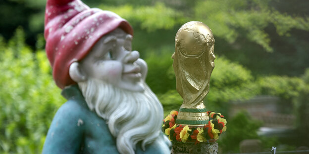 Ein nachgebildeter FIFA-WM-Pokal mit einer Girlande in den deutschen Nationalfarben und ein großer Gartenzwerg stehen im Vorgarten eines Hauses Ein nachgebildeter FIFA-WM-Pokal mit einer Girlande in den deutschen Nationalfarben und ein großer Gartenzwerg stehen im Vorgarten eines Hauses