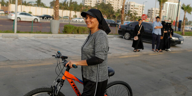 Saudi-Arabien: Frau geht mit ihrem Fahrrad an Palmen vorbei Saudi-Arabien: Frau geht mit ihrem Fahrrad an Palmen vorbei