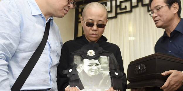 Liu Xia trägt eine Sonnenbrille und ein Bild von Liu Xiabo in der Hand Liu Xia trägt eine Sonnenbrille und ein Bild von Liu Xiabo in der Hand