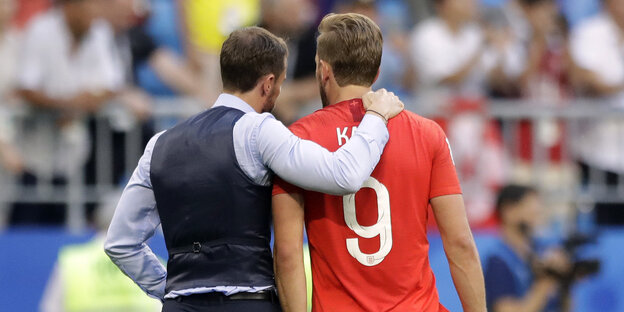 ein Mann mit Weste legt den Arm um die Schulter eines Fußballspielers