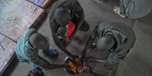 Von Libyen und Italien nicht erwünscht: Afrikanische Flüchtlinge teilen sich eine Schale mit Essen in einem Flüchtlingslager in Tripolis Von Libyen und Italien nicht erwünscht: Afrikanische Flüchtlinge teilen sich eine Schale mit Essen in einem Flüchtlingslager in Tripolis