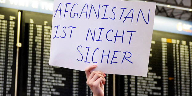 Vor einer Anzeigewand am Flughafen wird ein Schild hochgehalten: „Afghanistan ist nicht sicher“ Vor einer Anzeigewand am Flughafen wird ein Schild hochgehalten: „Afghanistan ist nicht sicher“